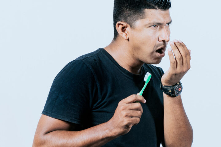 man checking for fresh breath wearing Invisalign with toothbrush